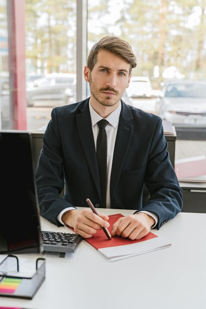 Professional businessman in suit sitting at a desk, pen in hand, serious expression, office environment.